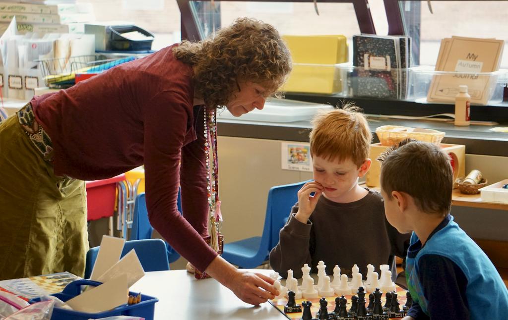 Teacher playing chess with two small boys